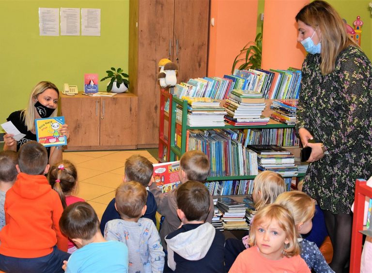 na zdjęciu widać panią bibliotekarkę mówiącą do dzieci i trzymającą w ręku książkę z boku stoi pani.