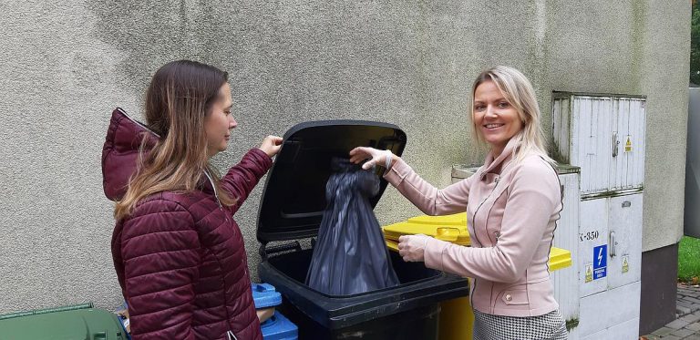 Dwie panie wyrzucają worek do śmietnika .