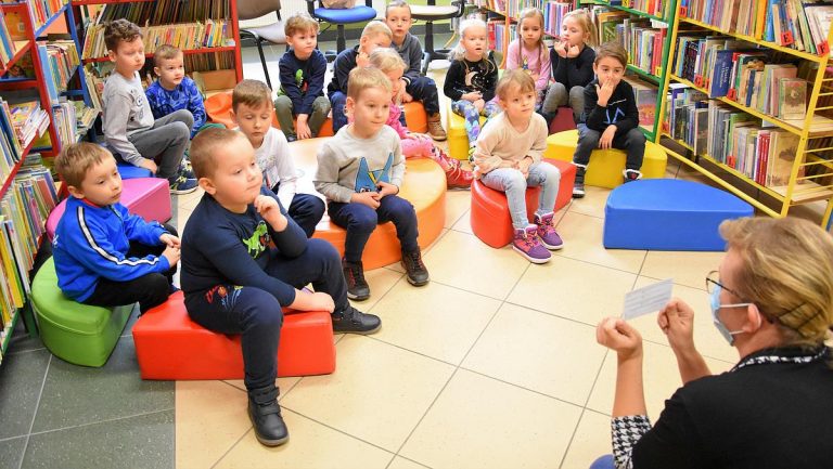 Grupa dzieci przyglądająca się karcie zapisu do biblioteki którą trzyma bibliotekarka.