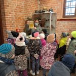 Grupa dzieci w budynku muzealnym oglądająca ulotkę, którą pokazuje pani.