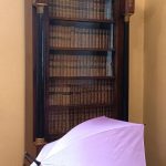 Na zdjęciu widzimy biblioteczkę wypełnioną książkami a przed nią ustawiony jest parasol z logo Gołdap Mazurski Zdrój.