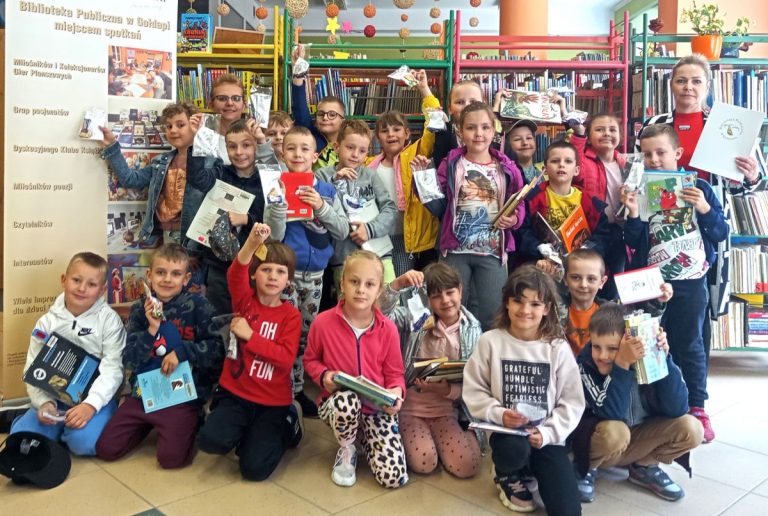 Na zdjęciu widzimy grupę dzieci z upominkami i książkami w ręku oraz panią wychowawczynię i panią bibliotekarkę.