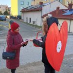 Czytelniczka odbiera książkę od pani z dużym sercem na plecach.