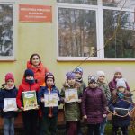 Grupowe zdjęcie opiekunki i dzieci które trzymają w rękach książki. Zdjęcie wykonane przed budynkiem odwiedzonej biblioteki