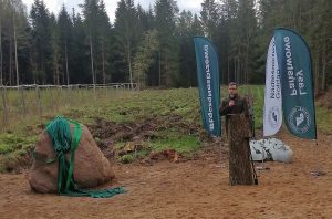 Pan przemawiający przez mikrofon na terenach leśnych.