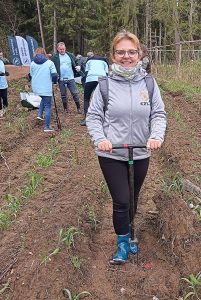 Pani w jasnej kurtce robiąca dziury do sadzenia drzew za tą panią inne osoby uczestniczące w akcji.