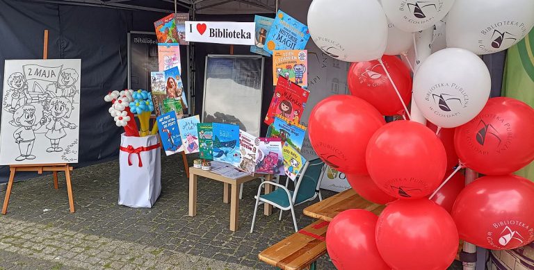 Stoisko biblioteki, balony białe i czerwone. W oddali widać dużą kolorowankę, kwiatki z balonów.