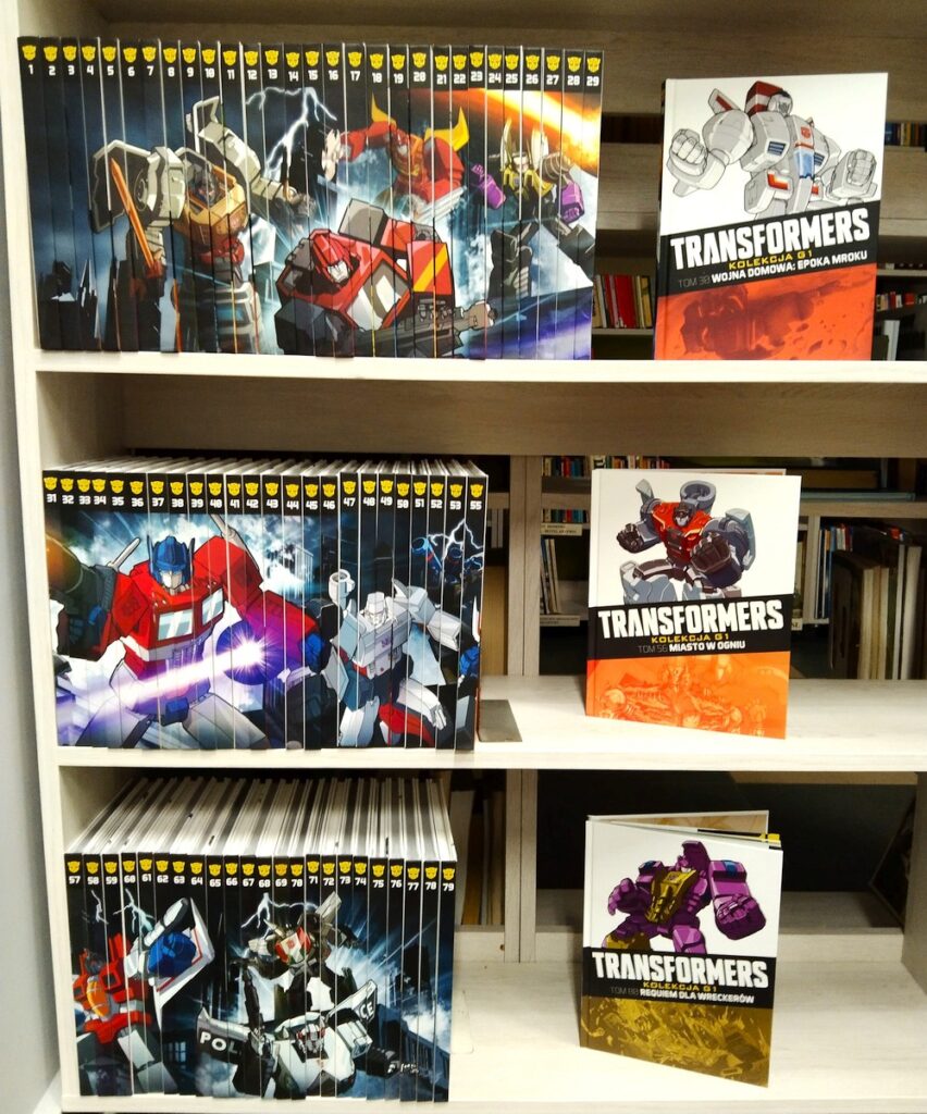 Książki – komiksy Transformers ustawione na trzech pólkach regału.