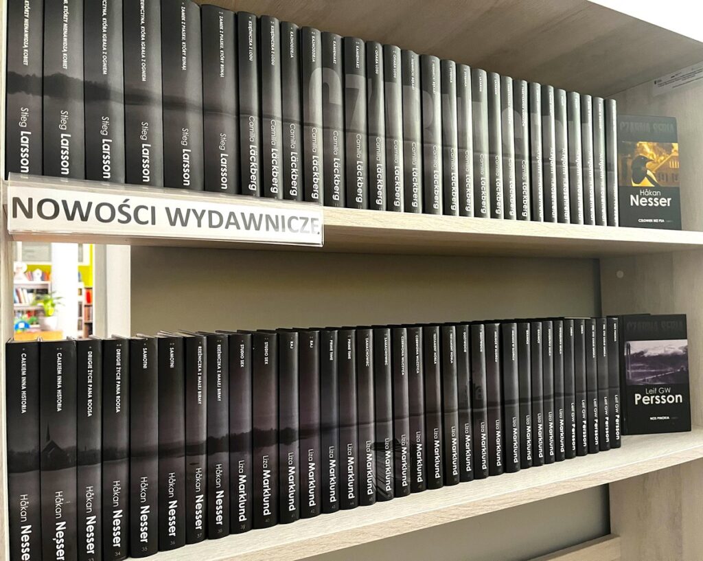 Seria kryminałów ustawiona na regale w wypożyczalni biblioteki.