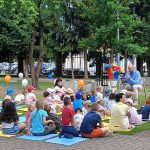 Pan siedzący przed grupą dzieci czyta książkę.