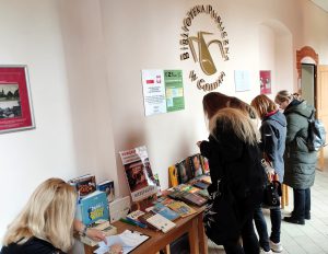 Uczestnicy wydarzeniu wybierają książki przygotowane w holu biblioteki podczas kiermaszu książki.