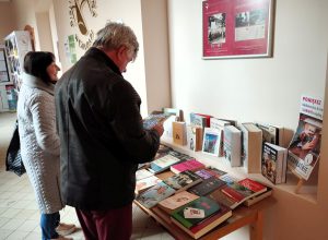 Uczestnicy wydarzeniu wybierają książki przygotowane w holu biblioteki podczas kiermaszu książki.