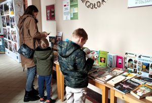 Uczestnicy wydarzeniu wybierają książki przygotowane w holu biblioteki podczas kiermaszu książki.