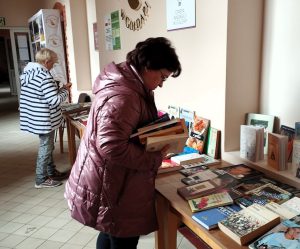 Uczestnicy wydarzeniu wybierają książki przygotowane w holu biblioteki podczas kiermaszu książki.