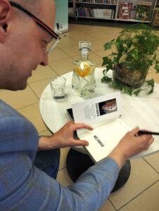 Na zdjęciu widzimy autora składającego autograf do książki.