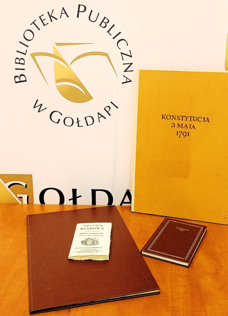 Na zdjęciu widnieje księga Konstytucja 3 maja, w tle logo biblioteki.