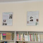Prace wiszą w antyramach nad regałami z książkami