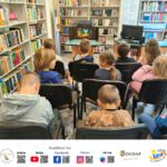 Grupa dzieci ogląda teatrzyk kamishibai. W tle widać regały z książkami.