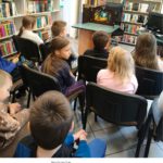 Grupa dzieci ogląda teatrzyk kamishibai. W tle widać regały z książkami.