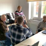Czworo uczestników warsztatów komputerowych rozmawiają ze sobą wymieniając się informacjami.