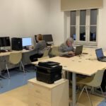 Pięć osób siedzi przy komputerach i zaabsorbowani w działanie ćwiczą.