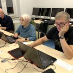 Troje starszych osób siedzą przy laptopach.