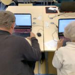 Dwie osoby siedzą przy laptopach i korzystają z programu do pisania.