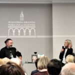 Na zdjęciu widzimy autorkę książek oraz prowadzącego przed nimi siedzą uczestnicy spotkania.
