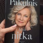 Na zdjęciu widzimy dłoń która trzyma książkę Marii Pakulnis "Moja nitka". Na okładce umieszczone jest zdjęcie autorki książki.