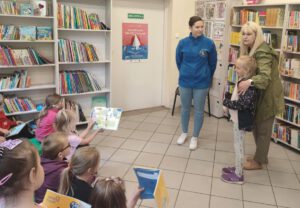 Dwie panie i dziewczynka stoją na tle regałów z książkami.