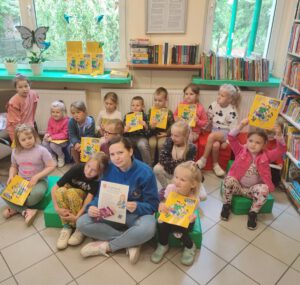 Dzieci z panią w niebieskim polarze siedzą na pufach pozując do zdjęcia