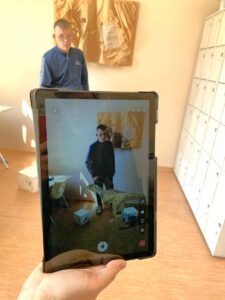 Na pierwszym planie tablet na którym widać uczestnika lekcji i stojącego przed nim dinozaura. Za tabletem tylko uczestnik (bez dinozaura) pozuje do zdjęcia.