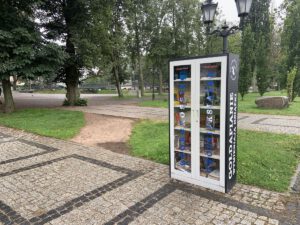 Zamknięta szafa bookcrossingowa na tle parku w centrum Gołdapi.