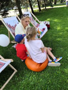 Kobieta siedząca na leżaku czyta dzieciom książkę.