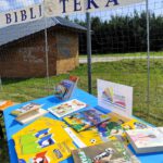 Ksiązki ułożone na stole za stołem widnieje napis Biblioteka.