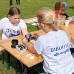 Pani w białej koszulce przykleja szablon tatułażu dzieczynce na rękę.
