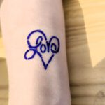 Na stole położona ręka na której wykonany jest tatułaż w kształcie serca.
