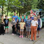 Dzieci stoją na tle samochodu straży granicznej z funkcjonariuszem jego psem.
