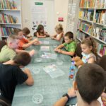 Dzieci siedzą przy stole i robią bransoletki z koralików.