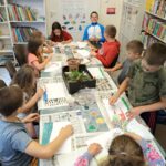 Dzieci siedzą przy stole i malują farbami.