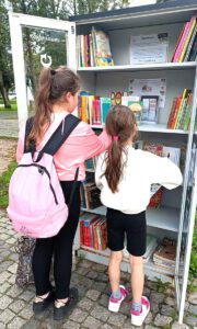 Fotografia przedstawia otwarta szafę bookrosingową i dziewczynki przeglądające książki