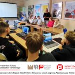 Grupa młodzieży siedząca za stołem ustawionym w podkowę.
