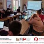 Młodzież pracująca na komputerach ustawionych na stołach.
