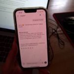 Telefon komórkowy na którym widnieje fraszka, w tle widać komputery.