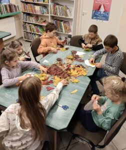 Dzieci tworzą pracę plastyczną z kolorowych, jesiennych liści.