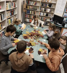 Dzieci tworzą pracę plastyczną z kolorowych, jesiennych liści.