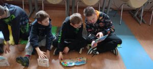 Trzech chłopców w wieku szkolnym siedzi na piankach wspólnie czytają i oglądają kolorowe książki