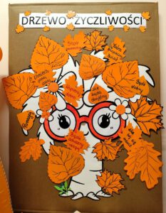 Drzewo życzliwości- zarys drzewa przypięty do tablicy korkowej. Drzewo ma nałożone pomarańczowe okulary oraz doczepione pomarańczowe liście.