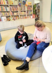 Mama z chłopcem wykonują pracę na szydełku siedząc na pufie.