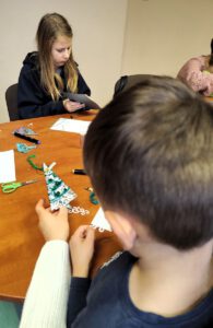 Uczestnicy warsztatu, jedna w dłoni trzyma zrobioną choinkę.